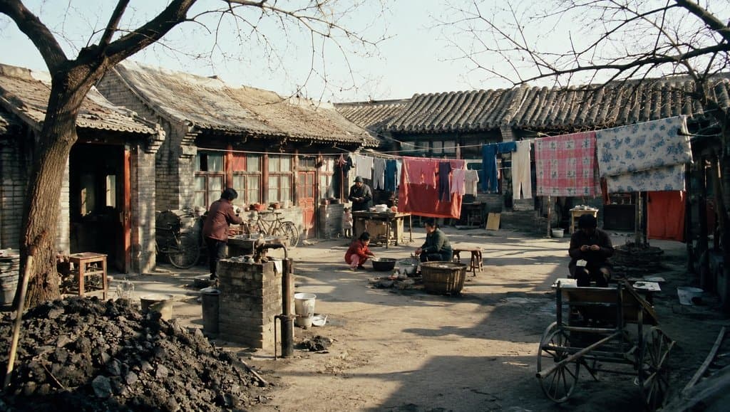 老北京大杂院场景，公用水龙头旁有人洗漱，煤堆、晾衣绳与传统房屋构成怀旧写实画面