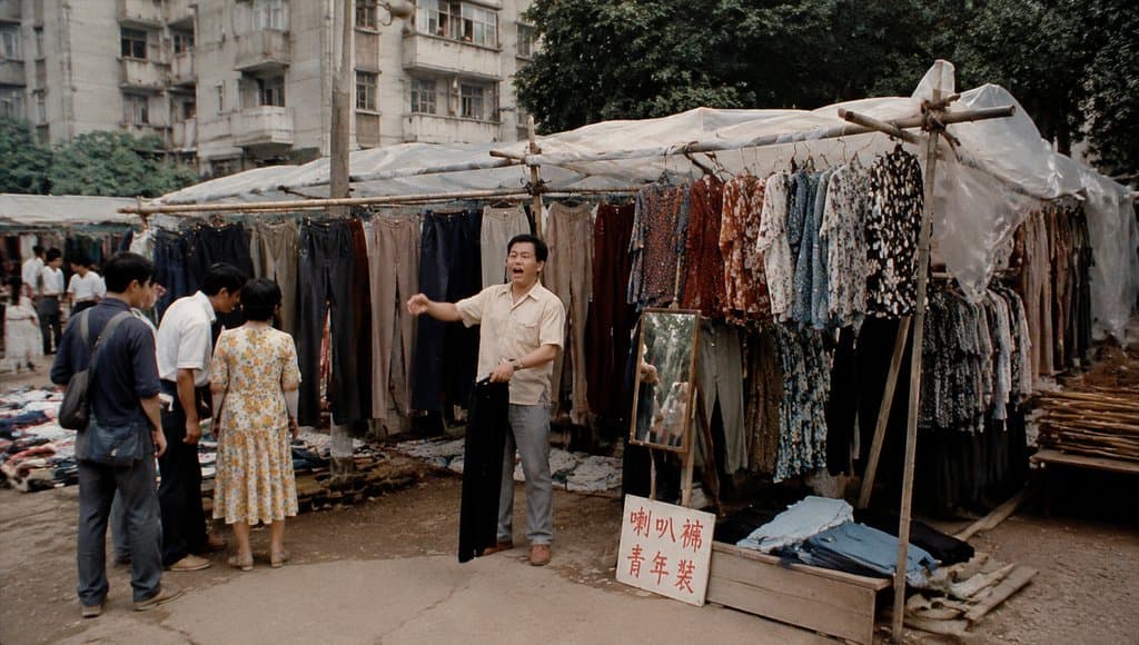 街头个体服装摊，挂满喇叭裤和青年装，塑料棚下设试衣镜，年代怀旧写实风格