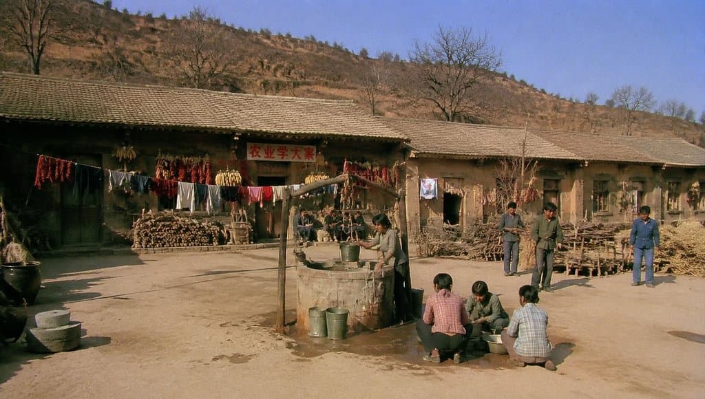 知青大院土坯房前，人们在公用井边洗衣，晾晒衣物与辣椒，年代怀旧写实场景