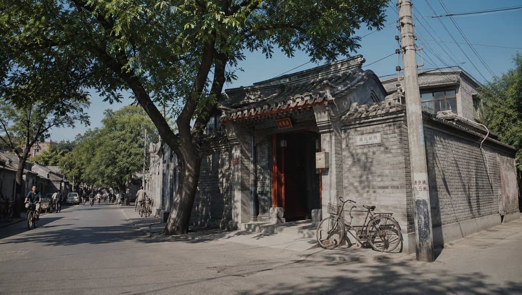 老北京胡同青砖灰瓦院门，槐树成荫，自行车停靠，怀旧写实风格