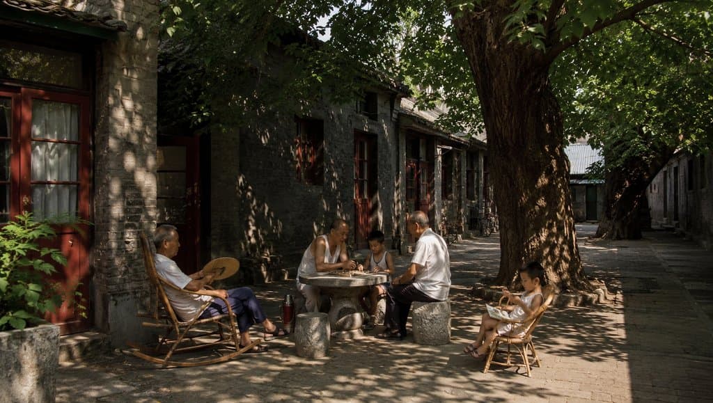 老院梧桐树下，几位老人与孩童在石桌旁乘凉下棋，光影斑驳，怀旧写实风格