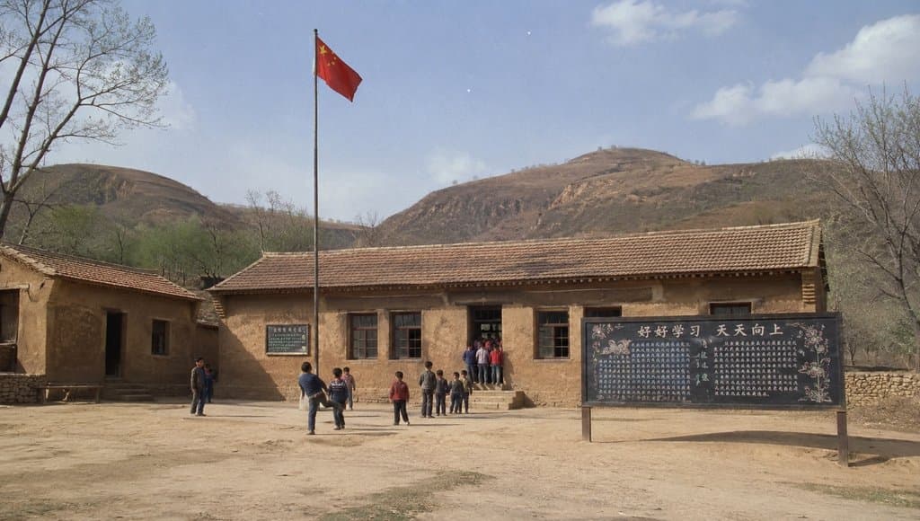 乡村小学土坯教室前，孩子们在旗杆下活动，黑板报写着‘好好学习 天天向上’，背景是黄土高原山丘，怀旧写实风格