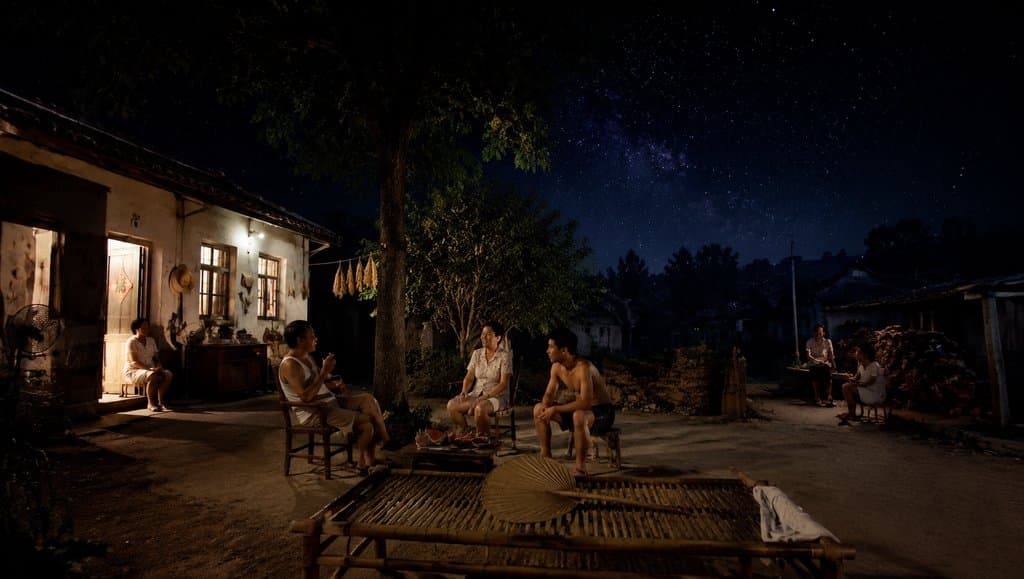 夏夜庭院中，家人围坐竹床蒲扇下乘凉，星空璀璨，怀旧写实风格