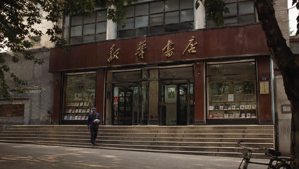新华书店门面，烫金店招，玻璃橱窗展示书籍，台阶前行人走过，年代感怀旧写实风格