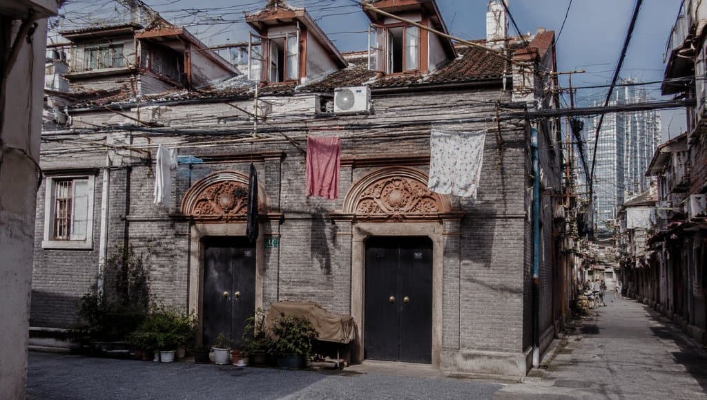石库门里弄老建筑，清水砖墙配黑漆门，老虎窗与悬挂衣物，年代怀旧写实风格