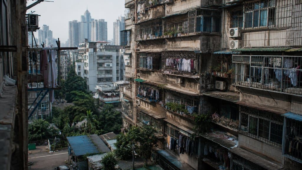 城中村老旧出租屋群，握手楼密集排列，阳台挂满衣物，背景现代高楼林立，写实都市风貌