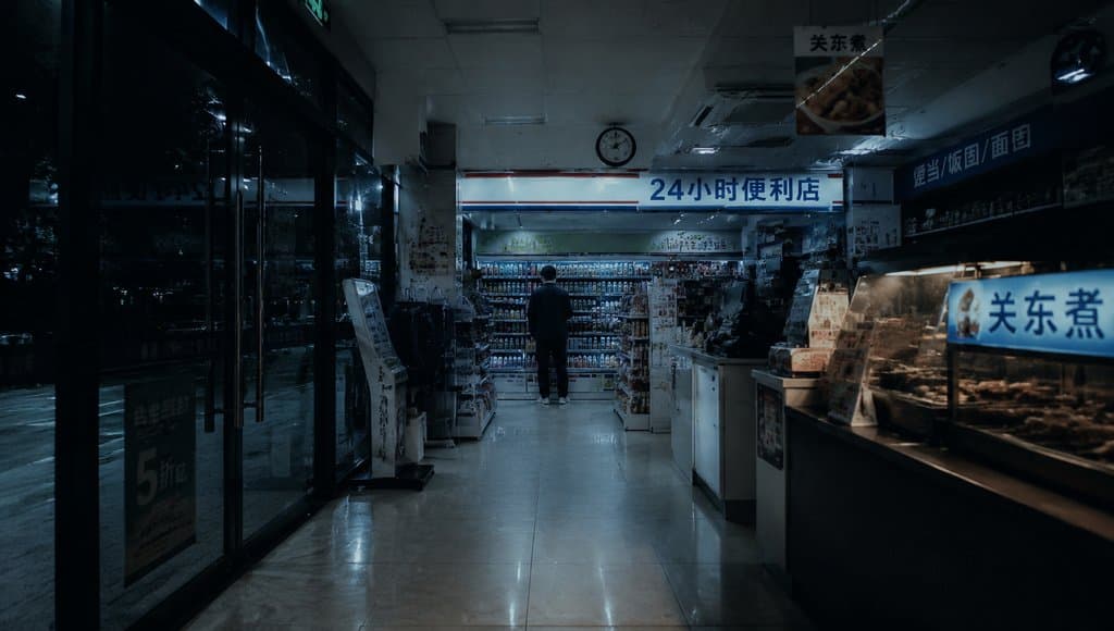 夜晚便利店内部，荧光灯照亮货架与收银台，一人背影伫立，现代都市写实风格