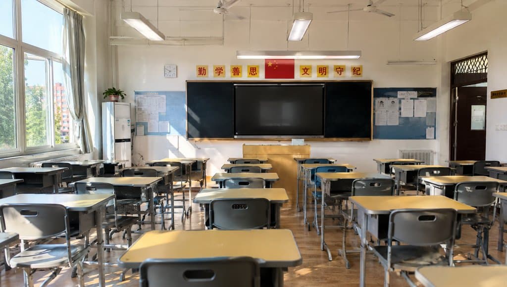 明亮的学校教室，成排课桌椅，黑板讲台，中国国旗和标语，现代都市写实风格