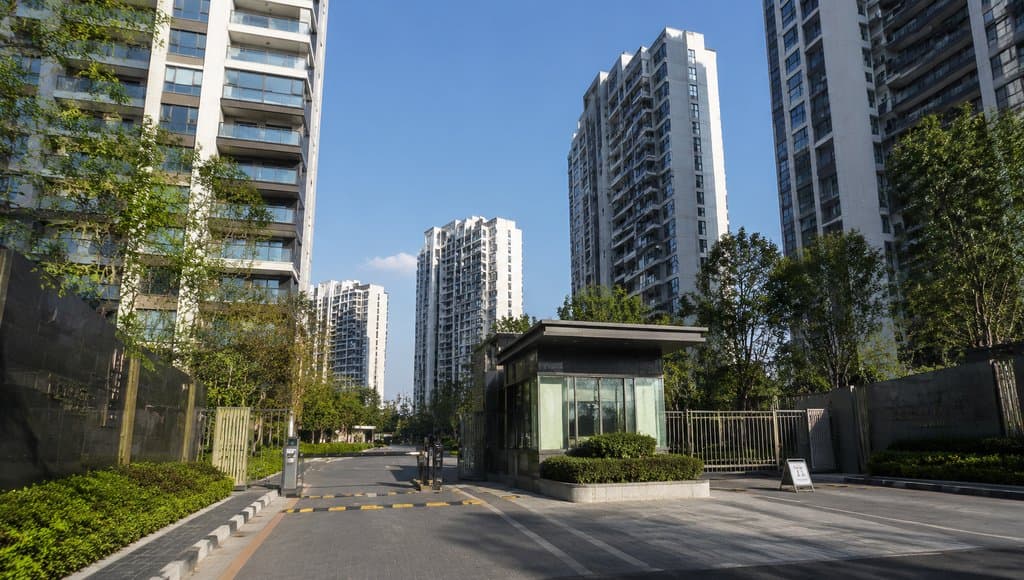现代城市住宅小区入口，高层建筑群环绕，绿植环绕，玻璃岗亭与自动道闸，写实风格